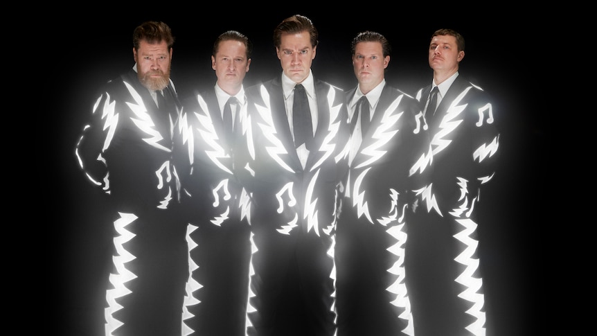 The Hives stand in matching black suits with reflector patterns of stripes and notes against black background