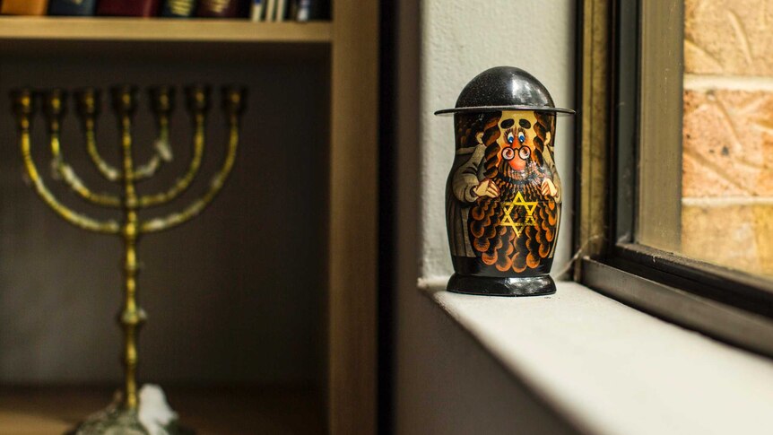 Jewish babushka doll beside window, and menorah on bookcase.