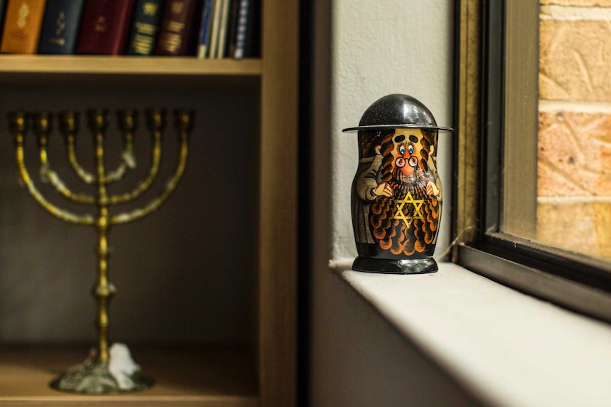 Jewish babushka doll beside window, and menorah on bookcase.
