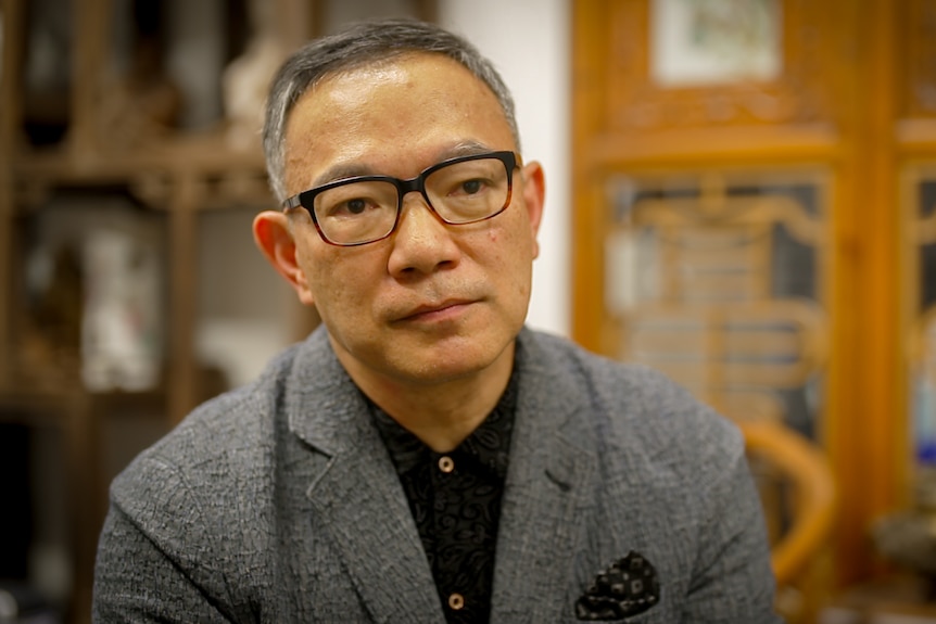 Paul Tse, wearing a grey suit jacket and glasses.