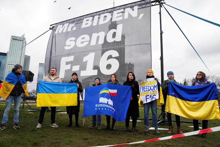 Protesters hold up Ukrainian flags in front of a big sign that reads, "Mr Bide, send F-16".