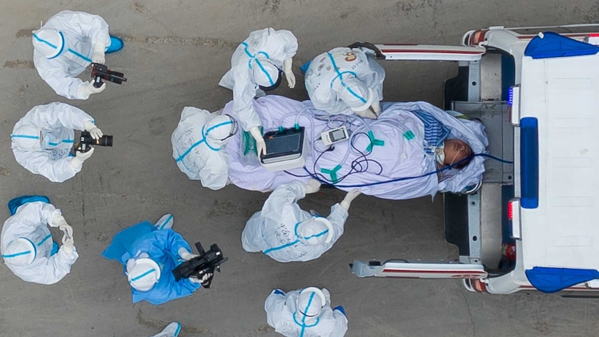 A photo taken from directly above shows a patient being loaded into an ambulance with medics wearing protective suits nearby.