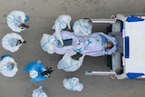 A photo taken from directly above shows a patient being loaded into an ambulance with medics wearing protective suits nearby.