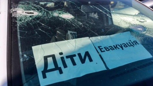 A car windscreen with holes in it, two pieces of paper have Ukrainian words printed on them.