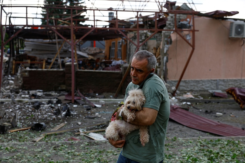 A man carries a dog past a building bombed out 