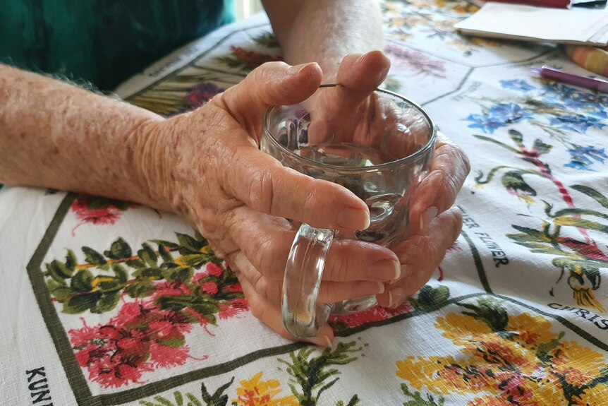 A close up picture of hands belonging to an older woman, grasping a glass mug.