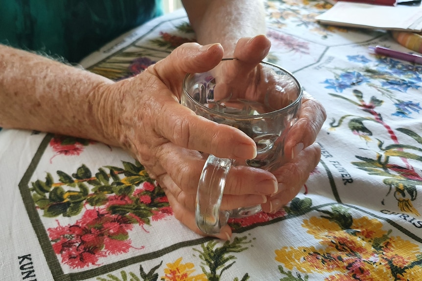 A close up picture of hands belonging to an older woman, grasping a glass mug.