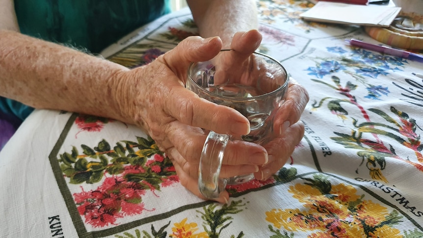 An older woman's hands grasping a glass mug.