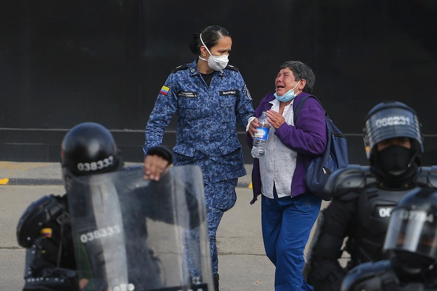 A woman cries walking on a road next to police guards in Colombia.