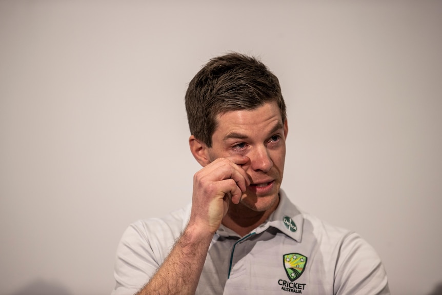 A man in a white polo shirt wipes his eye.