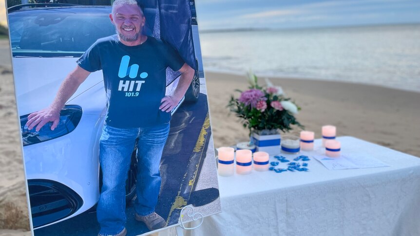 A photo of a man next to candles and flowers set on a table on the beach 