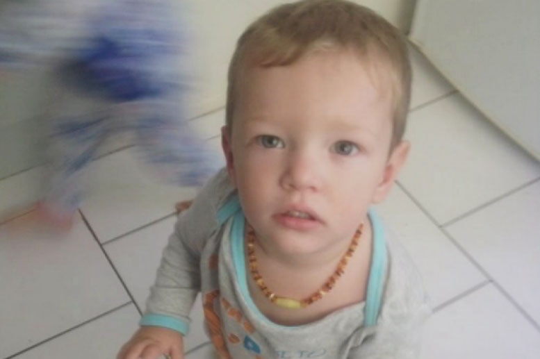 Toddler Mason Jet Lee looks up at the camera as he sits on a tiled floor.