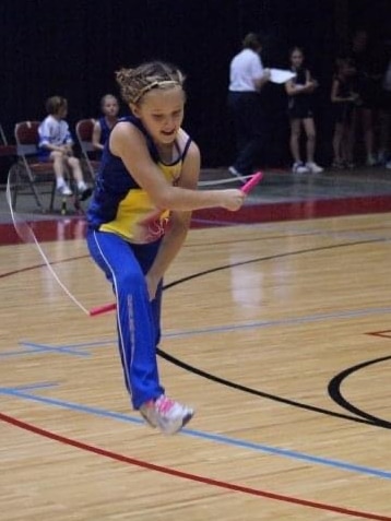 A young girl jumps over a skipping rope on a basketball court.