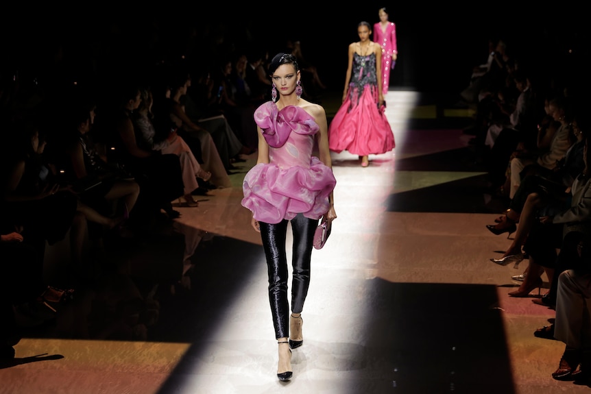 A model wearing a pink dress over shiny black pants. 
