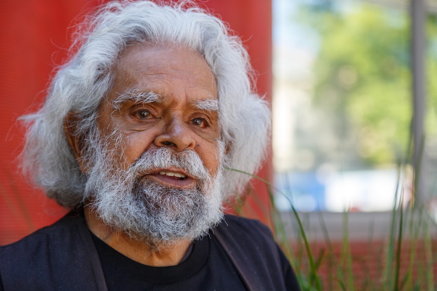 Uncle Jack Charles looks ahead thoughtfully as he sits outdoors on a sunny day.
