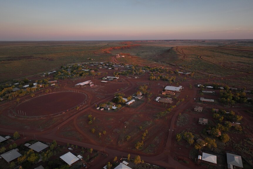 A drone shot from above showing the community of Balgo's few houses on red land near a vast escarpment.
