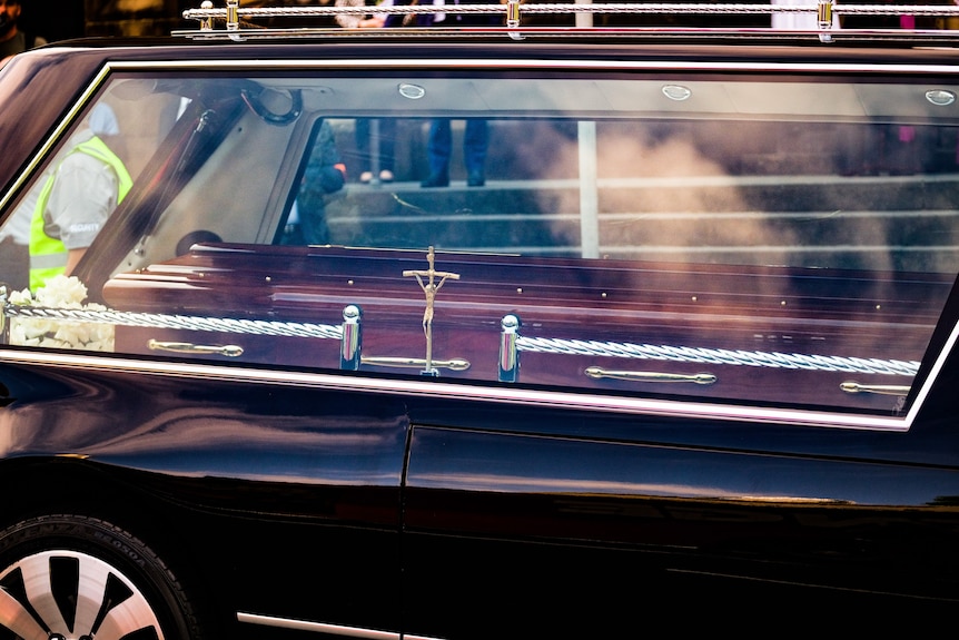 A coffin can be seen through the window of a hearse