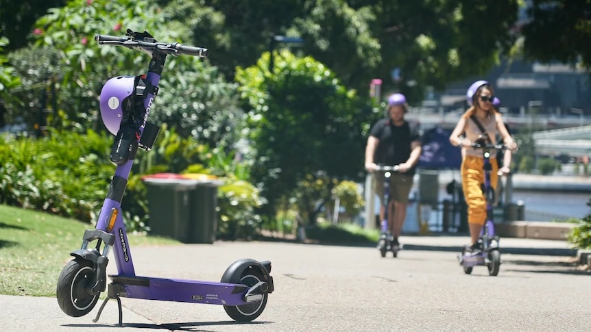 A bright purple motorised scooter sits to the right in the foreground with two people in the background