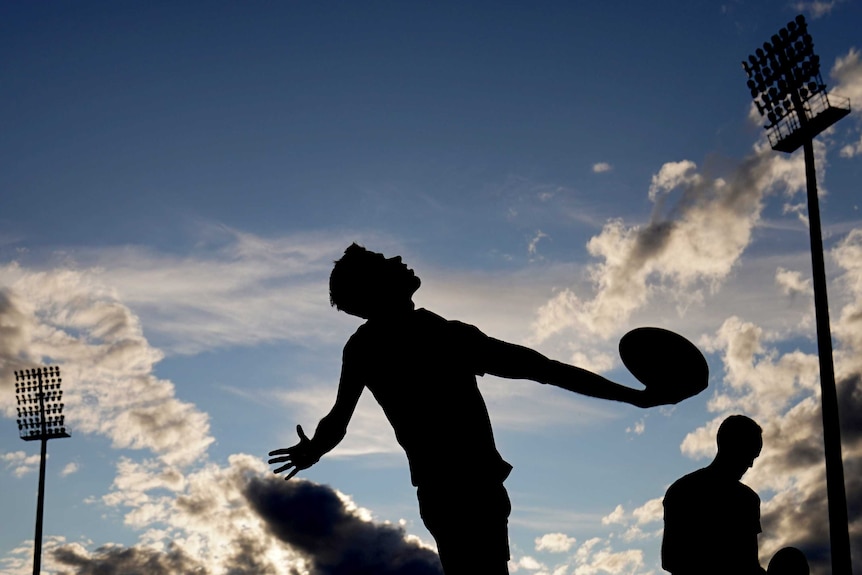 An Australian rules umpires prepares to throw the ball in from the boundary with his back turned to the players.