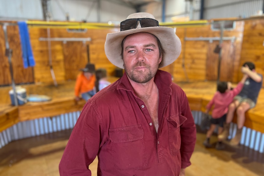 A man in a shearing shed with children playing in the background. 