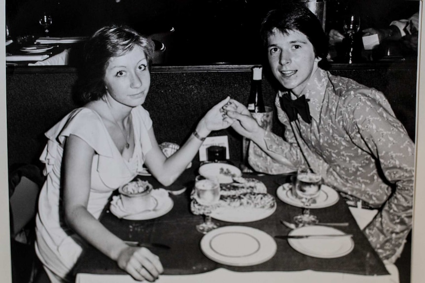 old black and white photograph of young couple at dining table holding hands