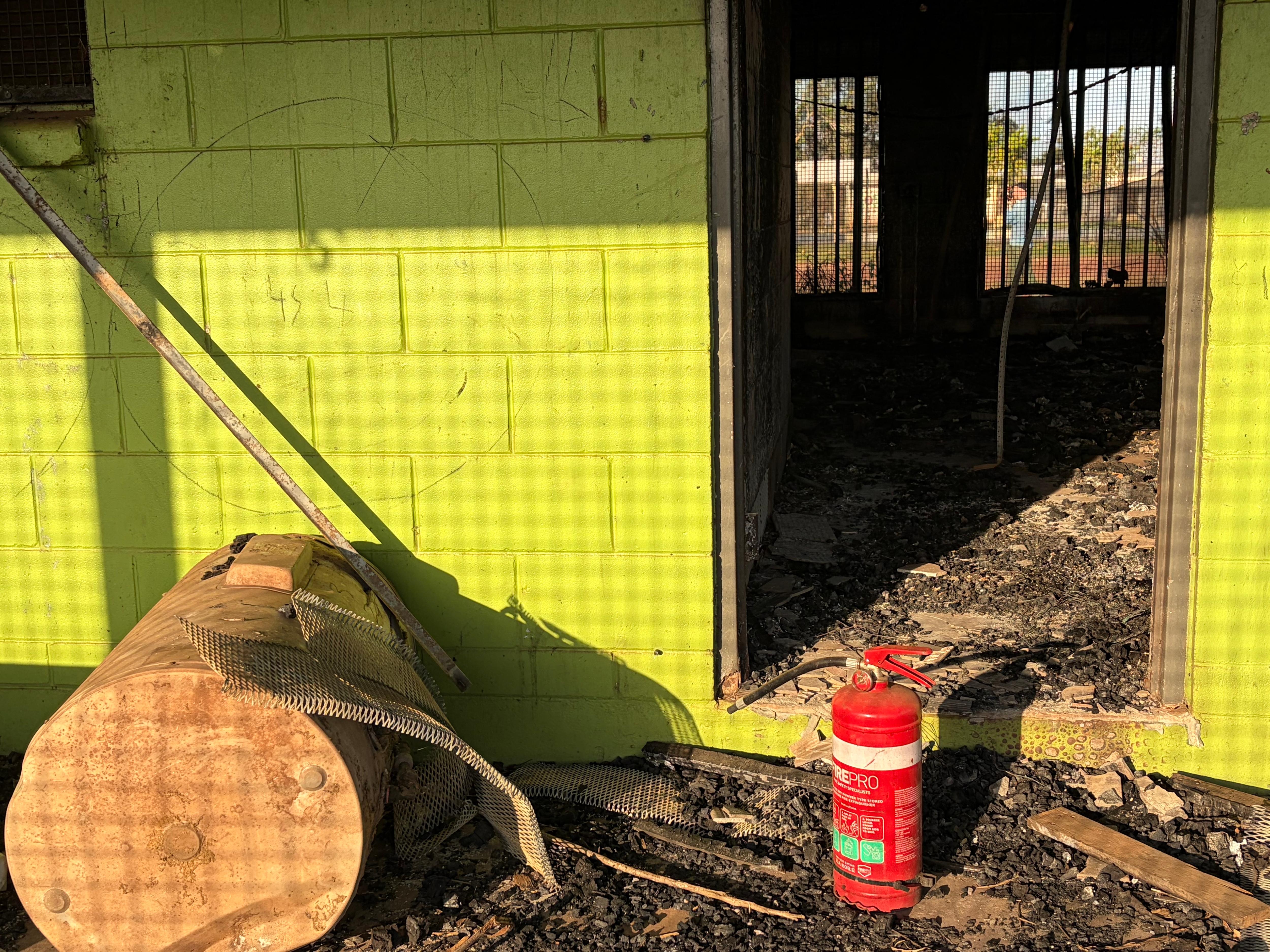 Green walls of a house looking in through a doorway to a burnt out home with a fire extinguisher in front