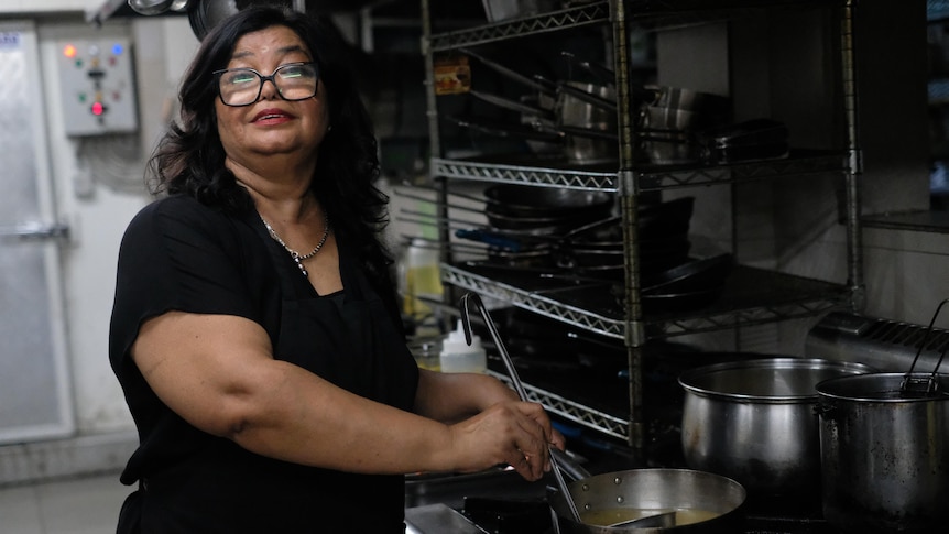 A woman stirs a pot in a commercial kitchen.