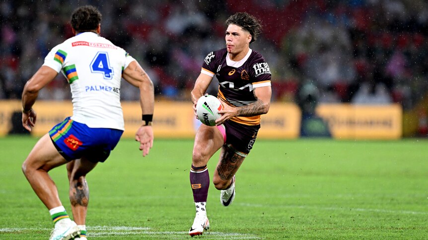 NRL player Reece Walsh running with the football in both hands, with one defender in front of him