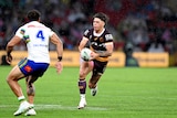 NRL player Reece Walsh running with the football in both hands, with one defender in front of him