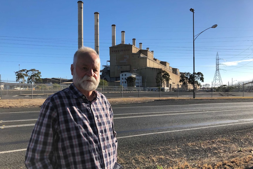 An older man with a beard stands in front of a power station