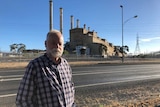 An older man with a beard stands in front of a power station