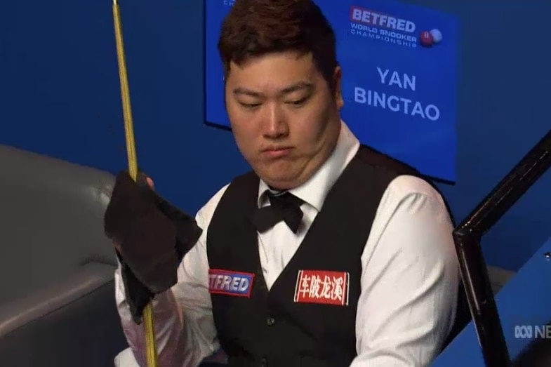 Yan Bingtao looks surprised while holding a snooker cue and rubbing it with a cloth