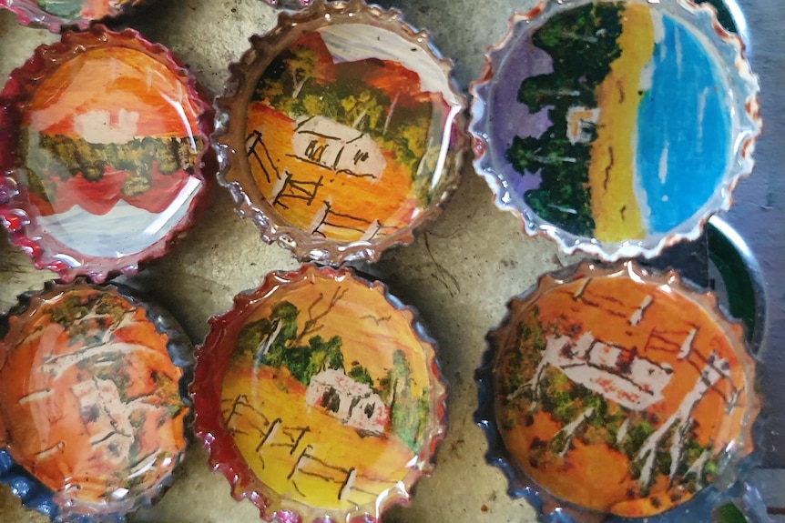 Close-up of six painted bottle tops with vibrant landscapes.