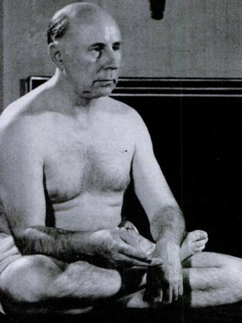 A Caucasian mature-aged man sits cross-legged with no shirt on.