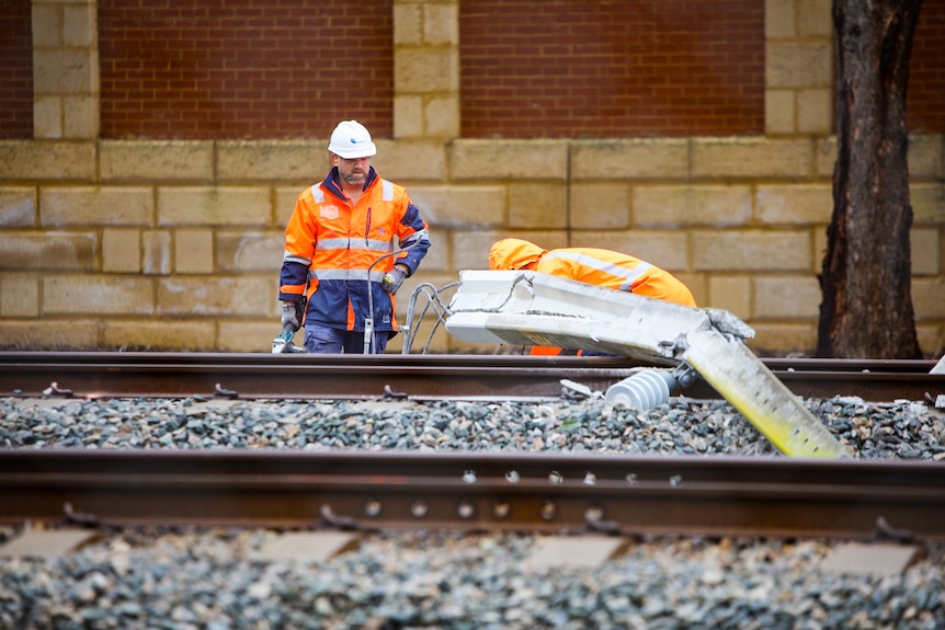 Workers in hi-vis clothing try to clear debris from train tracks.