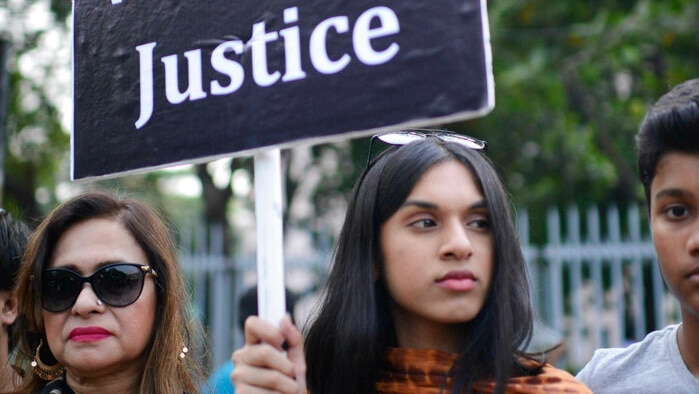 A young woman holds up a black sign that says "we want justice"