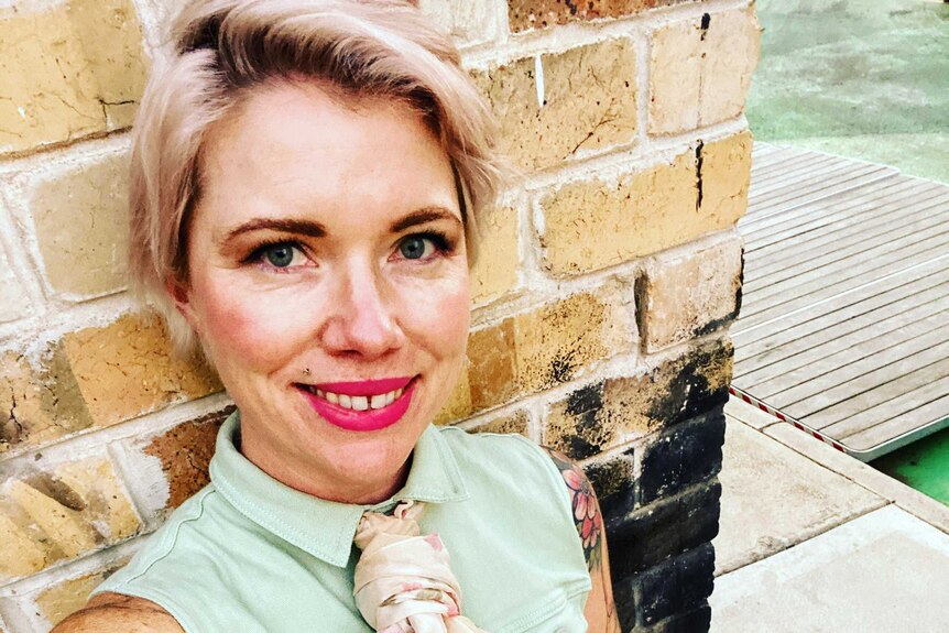 Clementine Ford takes a selfie while wearing a pale green jumpsuit and bright lipstick
