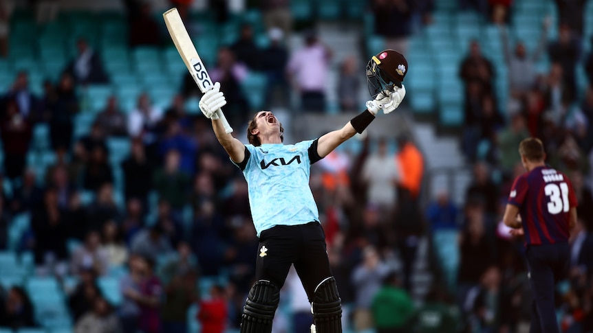 A man screams to the sky and lifts his bat in the air, celebrating a century.