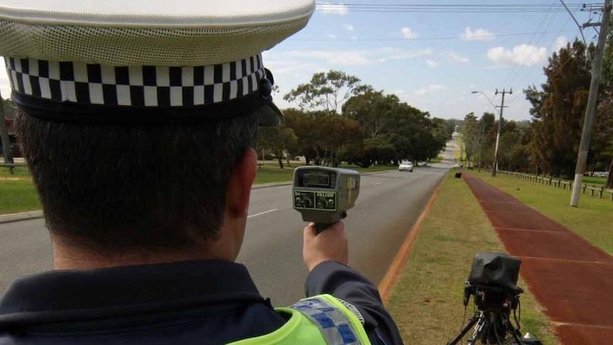 Behind shot of police officer holding a radar gun pointing down a road.