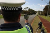 Behind shot of police officer holding a radar gun pointing down a road