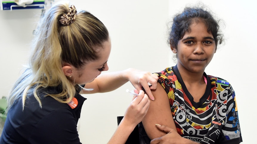 A young indigenous woman smiles while being vaccinated. 