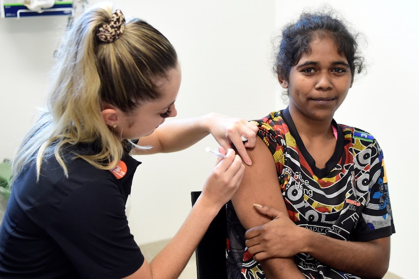 A young indigenous woman smiles while being vaccinated. 