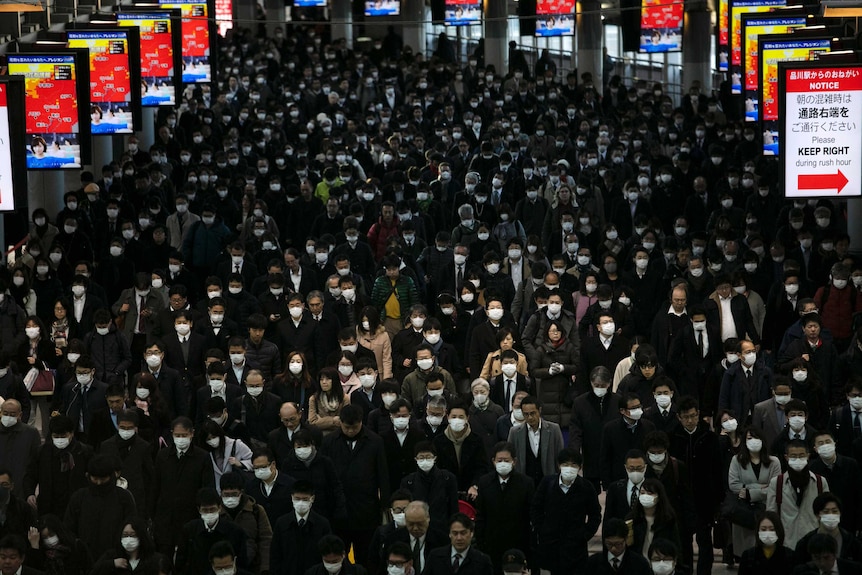 A large crowd wearing masks walks through the Shinagawa Station in Tokyo