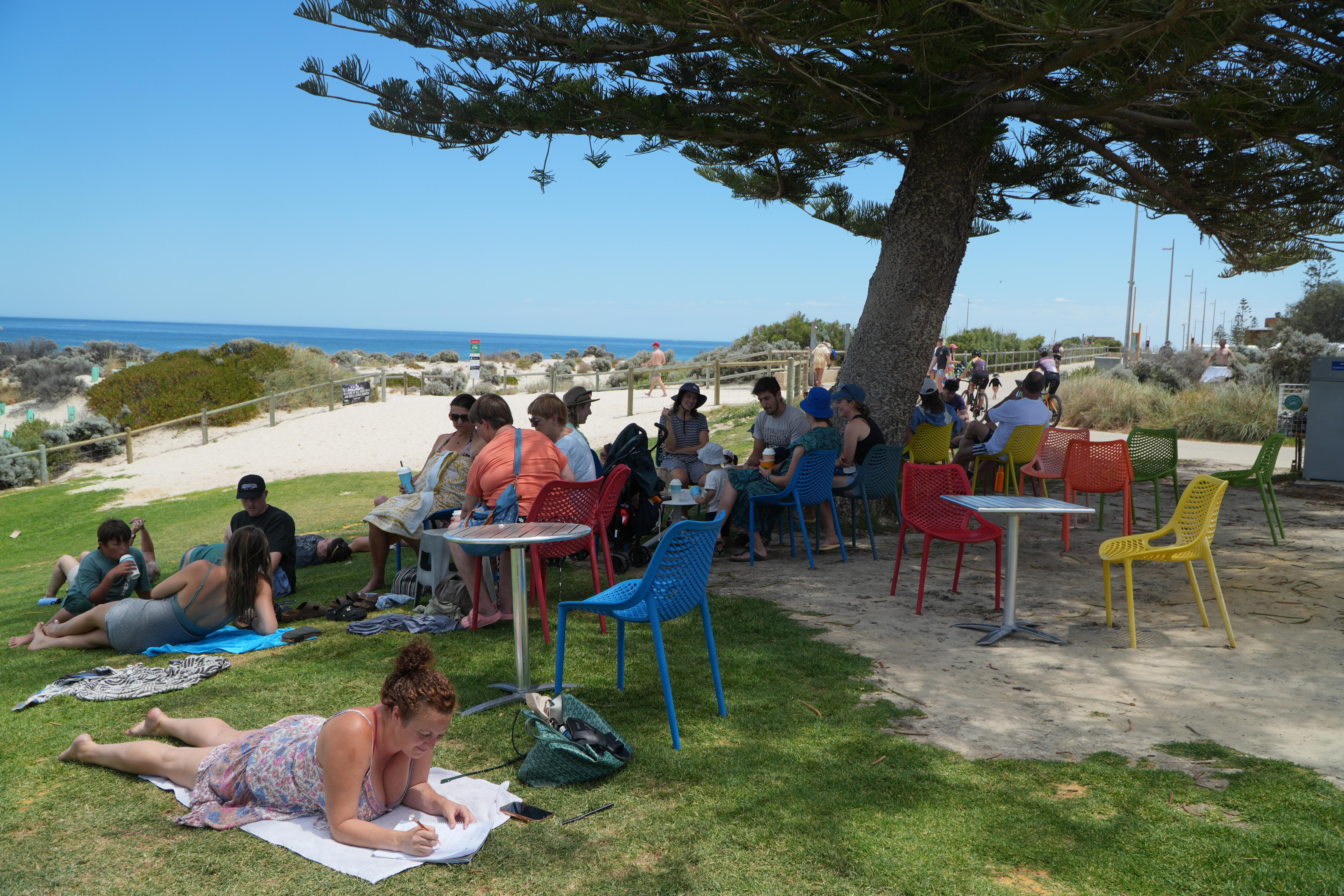 A crowd of individuals sitting on chairs or lying on the grass next to a beach.