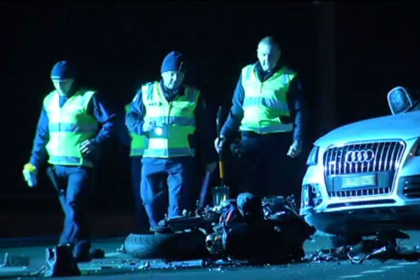 Three police officers walk past an Audi car and a destroyed motorcycle.