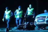Three police officers walk past an Audi car and a destroyed motorcycle