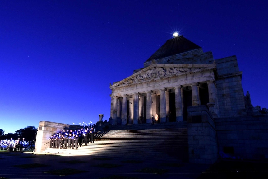 Wide view of the Shrine of Remembrance in Melbourne with people standing on the steps and the day breaking behind.