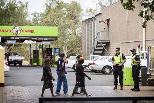 Police stand outside a bottle shop as people walk past in Alice Springs.