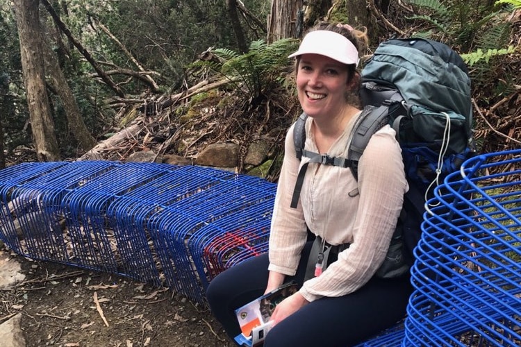 Lizzie Strick with a hiking backpack on sitting on a blue seat in a rainforest