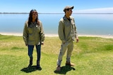 Two people are standing on a lakefront smiling and looking away from the camera.